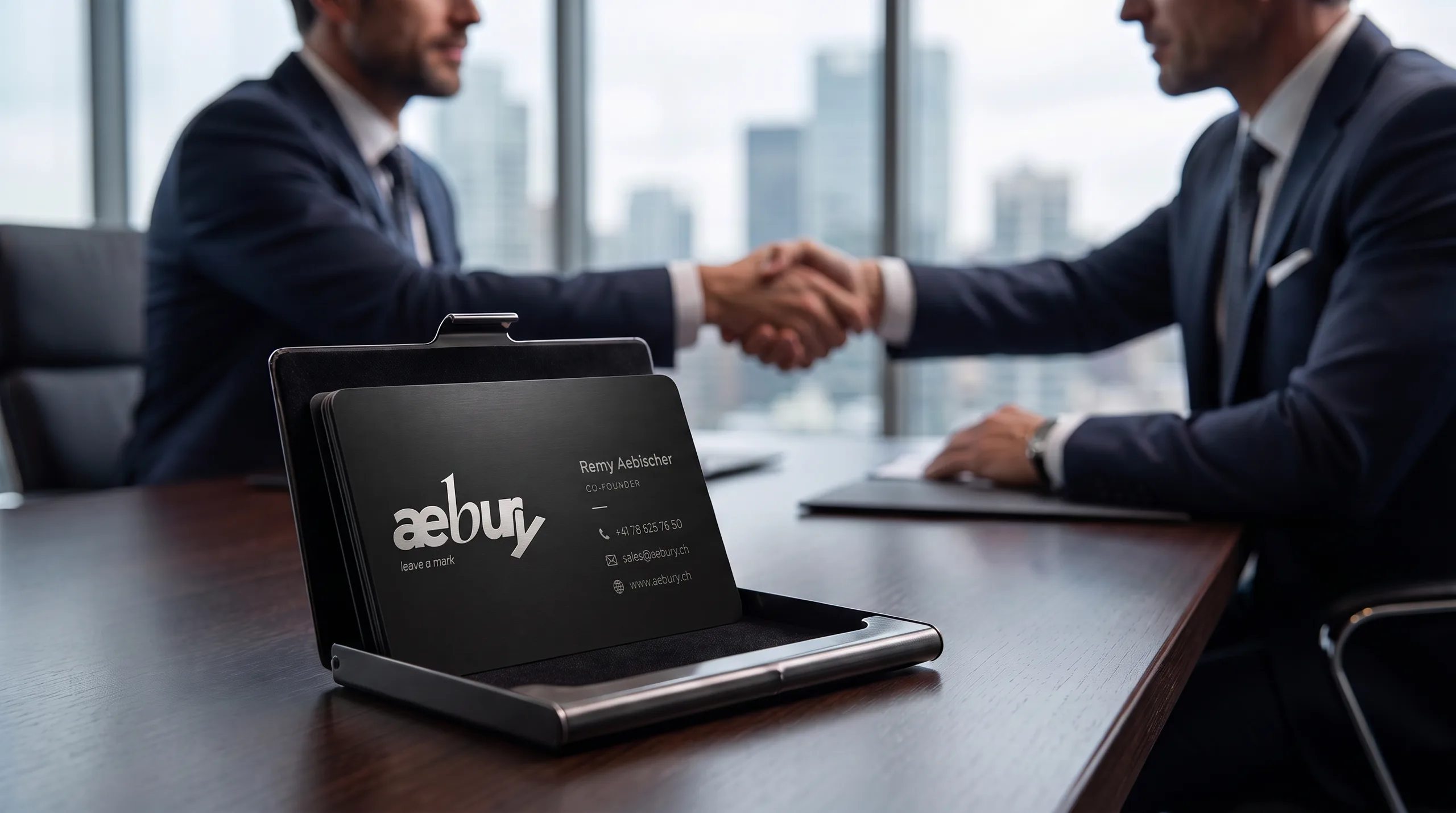 Aufgeklapptes Etui mit schwarzen Aebury-Karten auf dem Besprechungstisch, dahinter zwei Geschäftsleute beim Handschlag